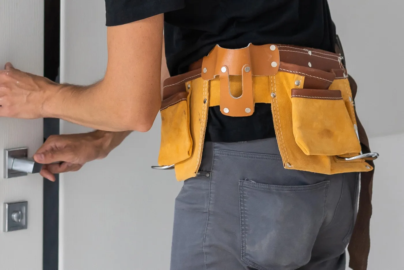Serrurier équipé de sa ceinture à outils devant une porte dans le 20e arrondissement de Paris